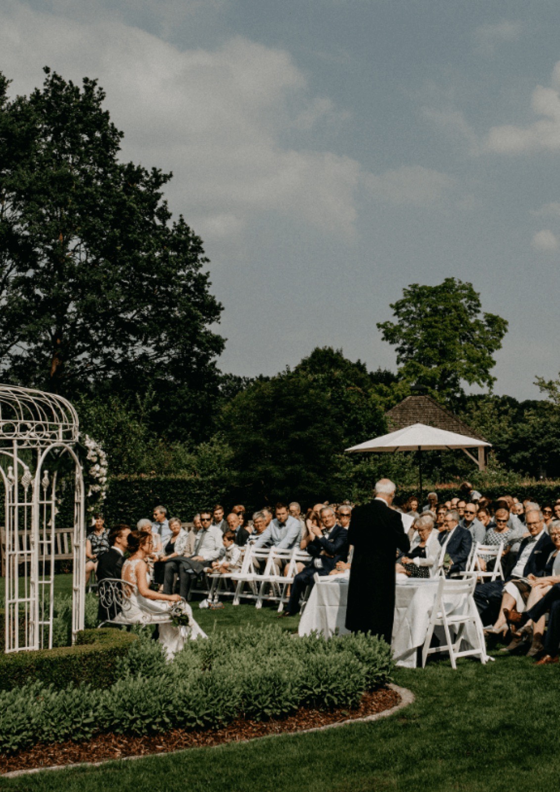 Huwelijksceremonie in de tuin van Hof te Rhode, met gasten op witte stoelen